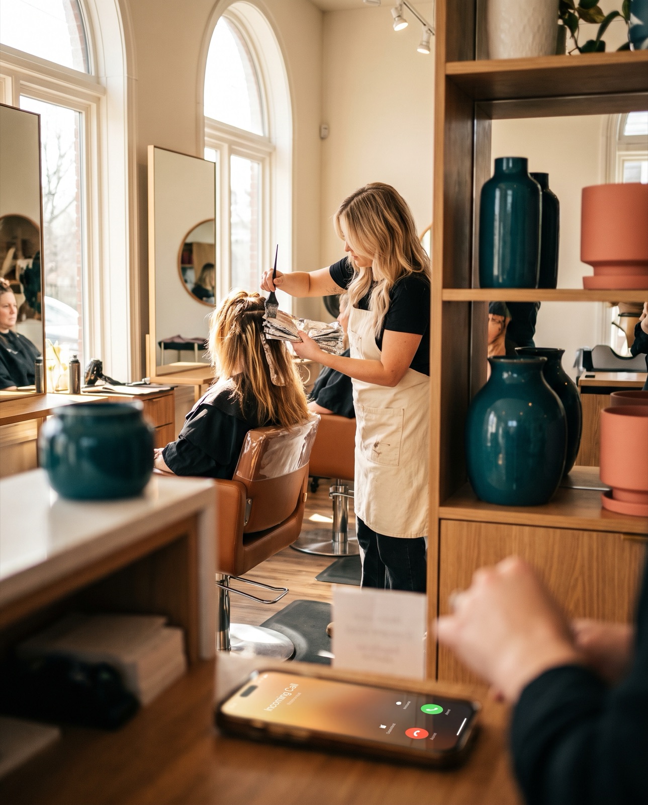 A stylist mid-foil with both hands full while the salon phone rings on the counter
